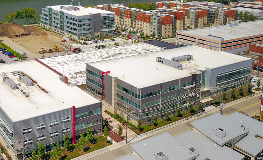 Aerial view of several modern commercial office buildings with flat roofs and nearby parking lots in an urban area.