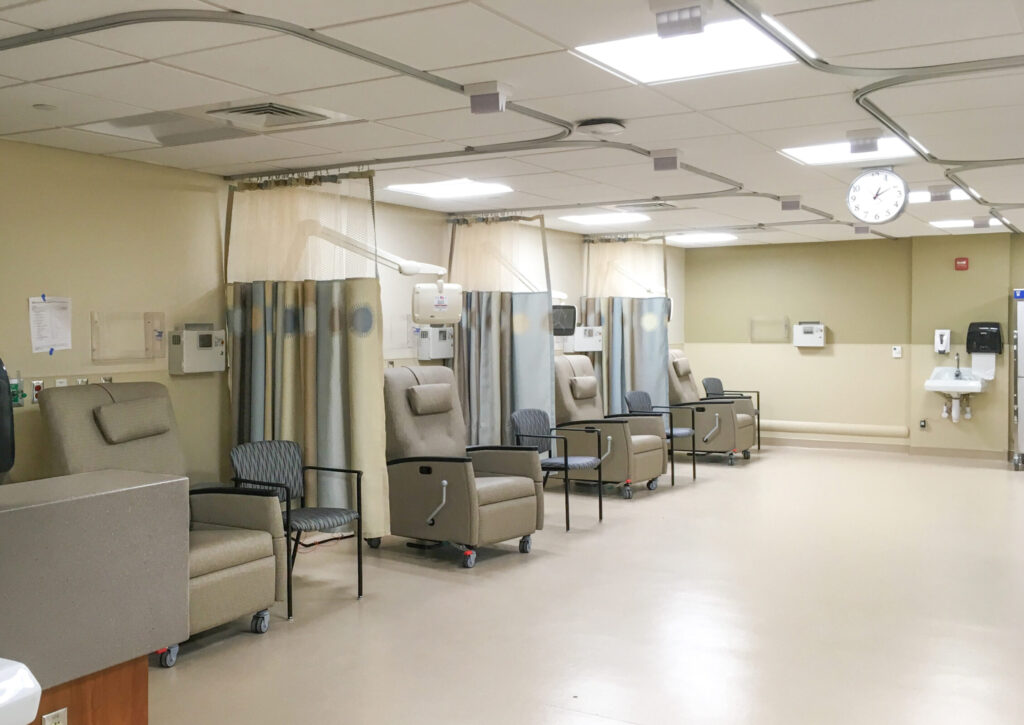 A medical infusion room with a row of reclining chairs and privacy curtains.