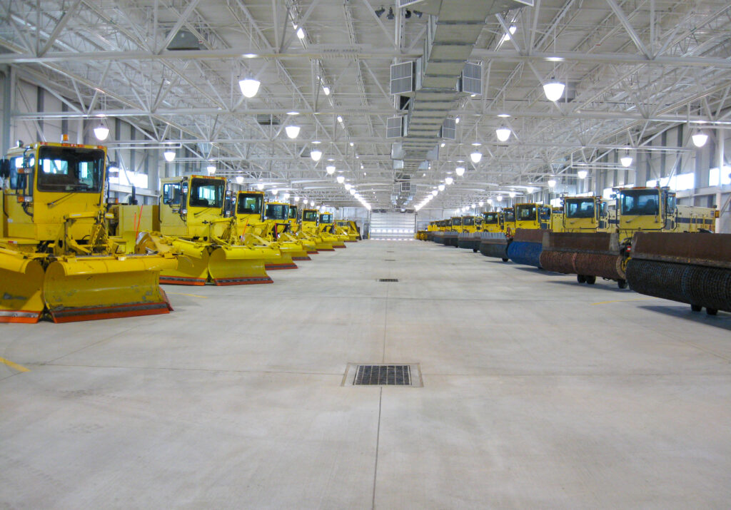Two rows of parked yellow snowplows inside a large maintenance garage.