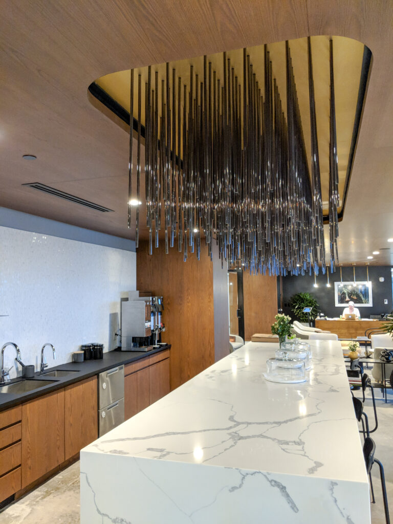 A long white marble kitchen island with a tiered hanging metal light fixture above it in a modern office space.