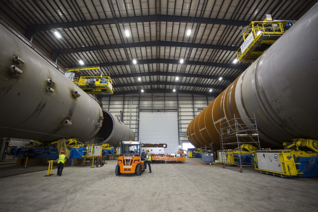 Two large industrial tanks under construction inside a warehouse with a forklift operating between them.