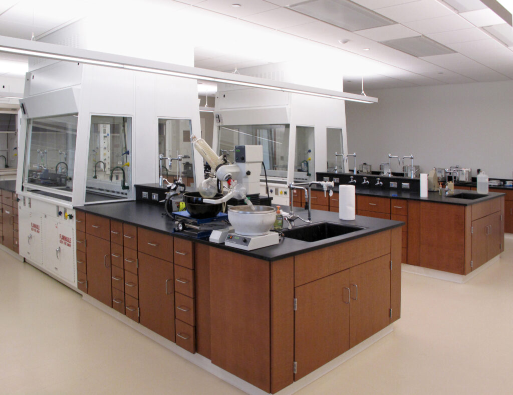 A chemistry laboratory with wood cabinets, black countertops, several fume hoods, and a rotary evaporator.