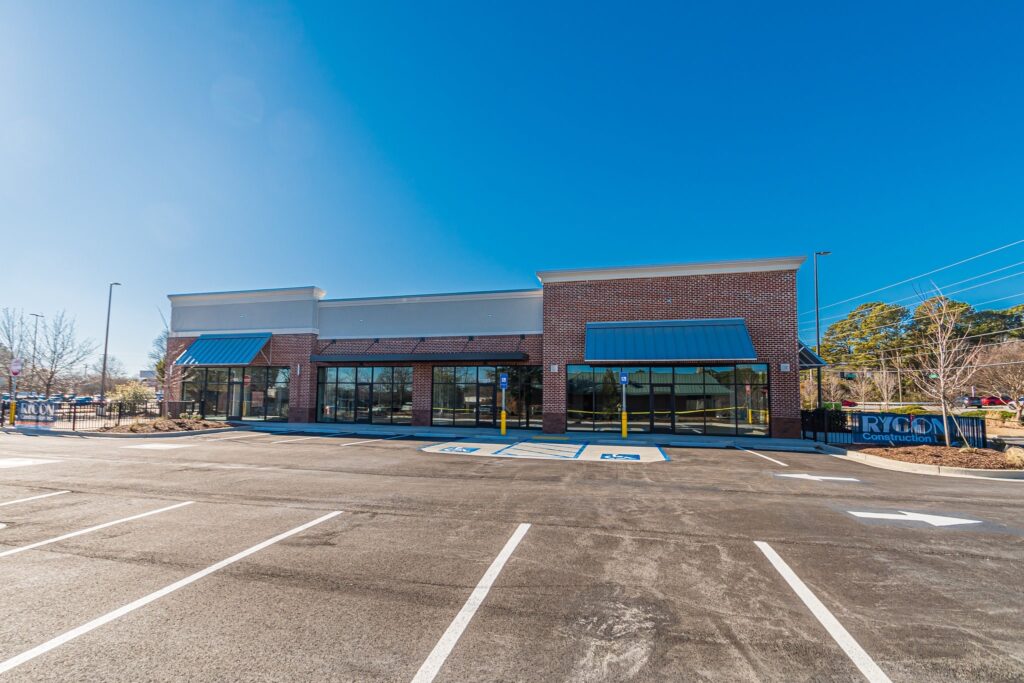 A vacant brick retail building with a large parking lot featuring marked handicap spaces.