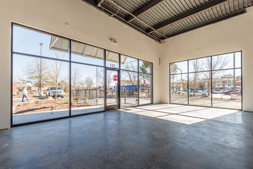 An empty commercial space with large glass windows looking out onto a parking lot.
