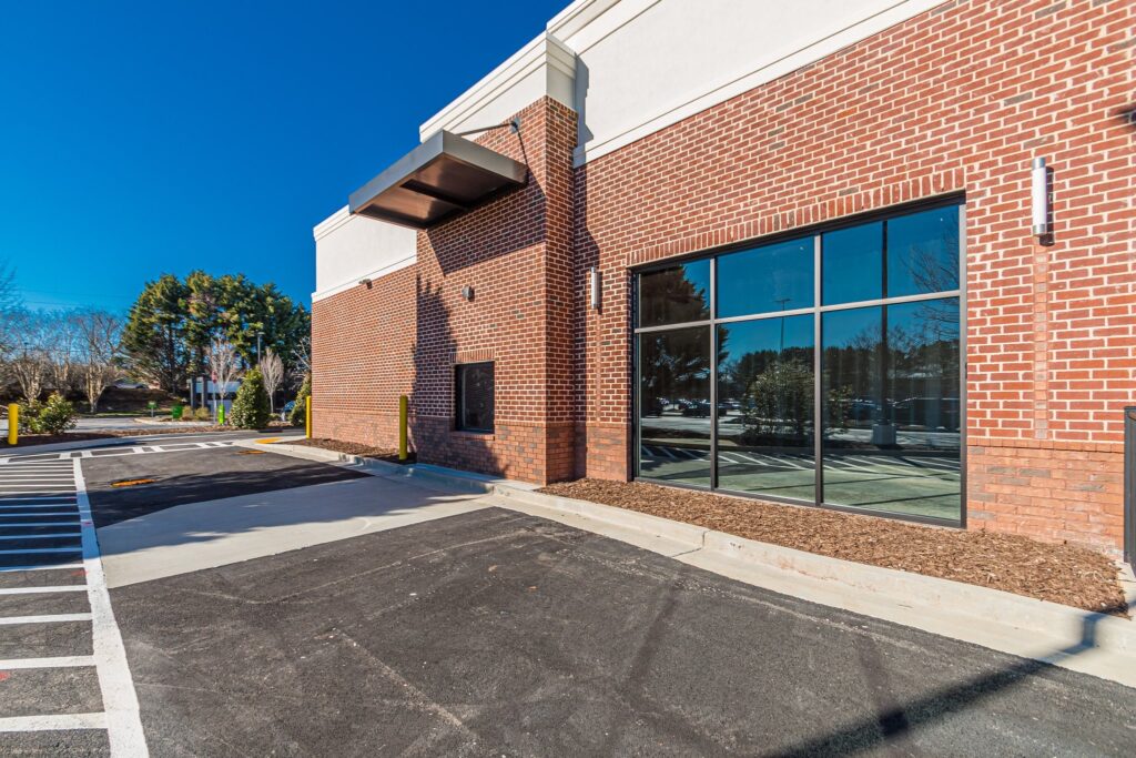 Exterior of a red brick commercial building with a drive-thru window and large glass storefront windows next to an asphalt parking lot.