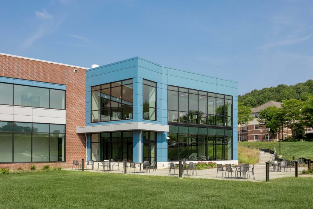 Modern brick and blue-paneled building with floor-to-ceiling windows and a patio with outdoor seating.