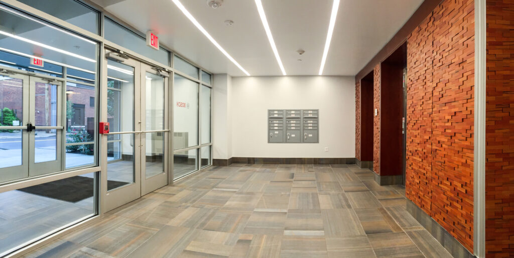 Modern building lobby with glass entrance doors, a bank of mailboxes on the back wall, and a textured wood-paneled feature wall.