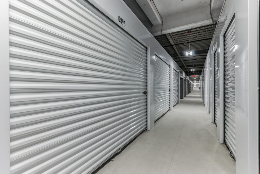 A hallway inside a self-storage facility lined with white roll-up metal doors.