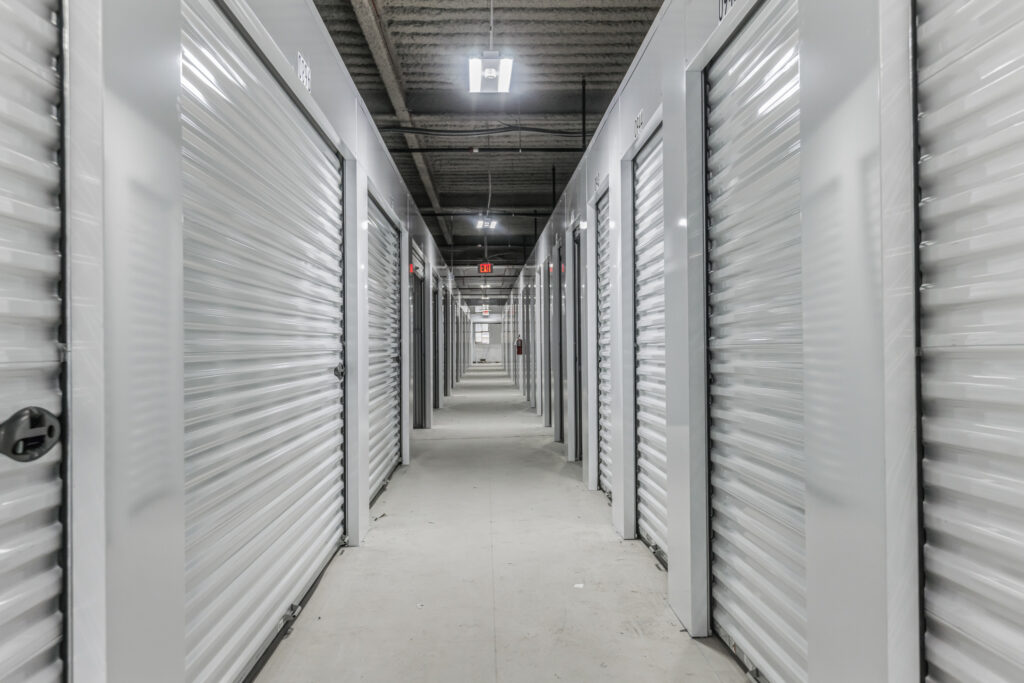 A hallway in a self-storage facility lined with white corrugated metal unit doors.