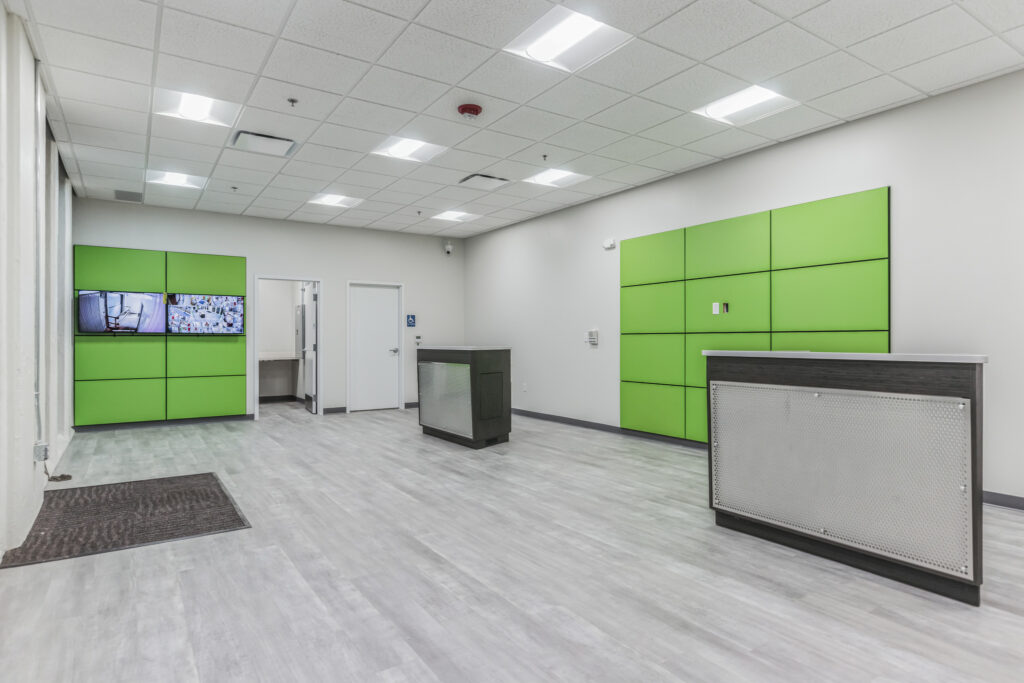 Empty office reception area with grey flooring, white walls, green accent panels, and two service desks.