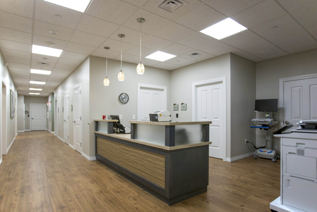 Reception area in a medical office with a wooden desk, pendant lights, and a hallway leading to doors.