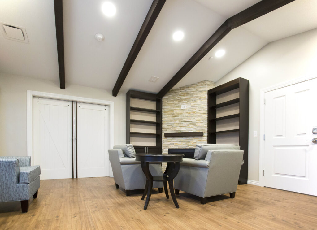 A room with two light blue armchairs, a small round table, built-in shelving, and a fireplace with a stone surround.