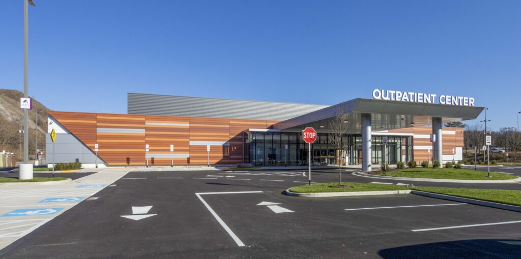 Exterior of a modern outpatient center with a covered entrance, parking lot, and stop sign.