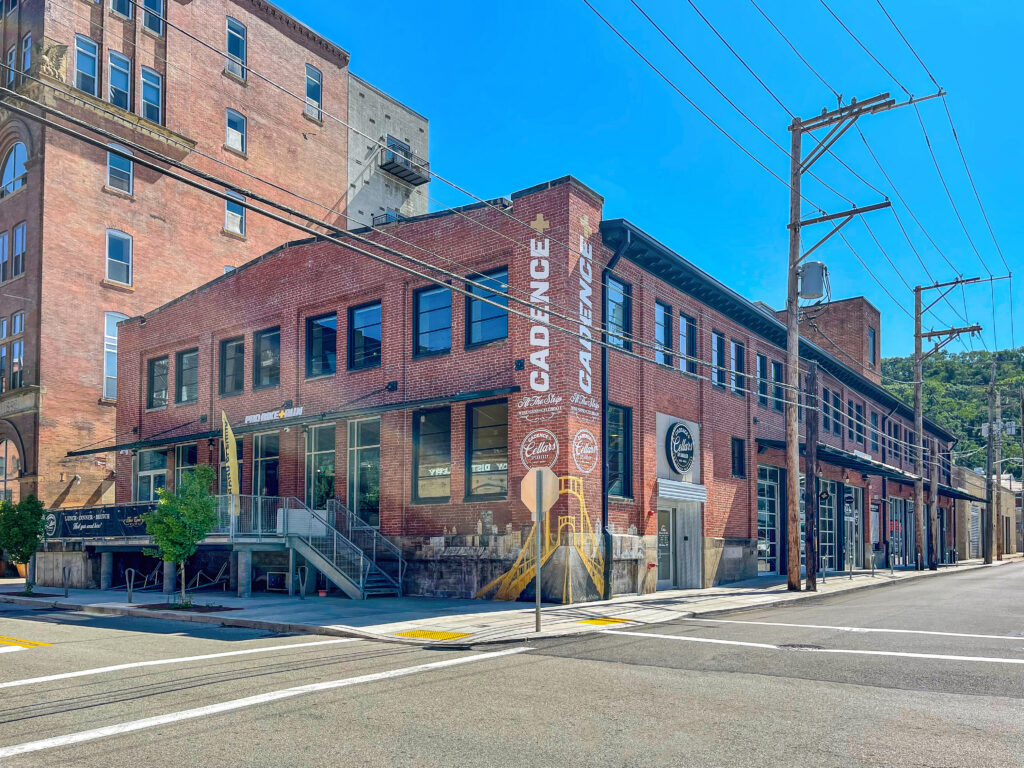 Red brick corner building featuring businesses labeled “Cadence” and “Pro Bike + Run” with a mural of a bridge on the side wall.
