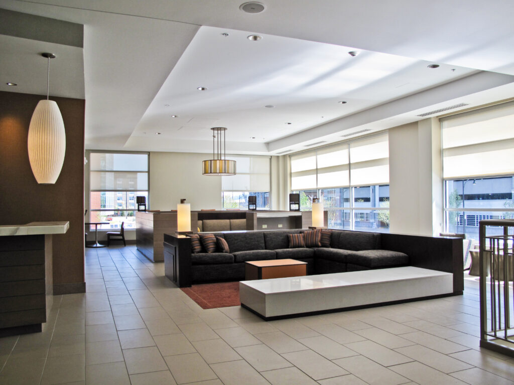 Modern hotel lobby with a large charcoal sectional sofa, a white coffee table, and tall pendant lights.