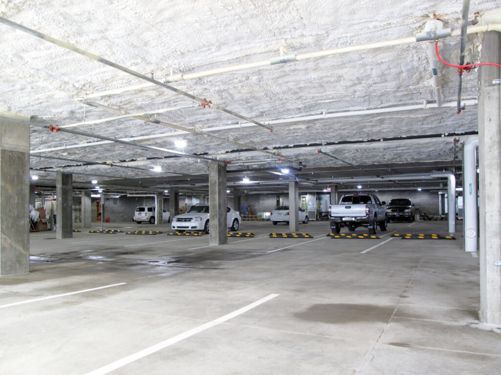 An indoor parking garage with concrete pillars, a textured ceiling, and several parked cars.