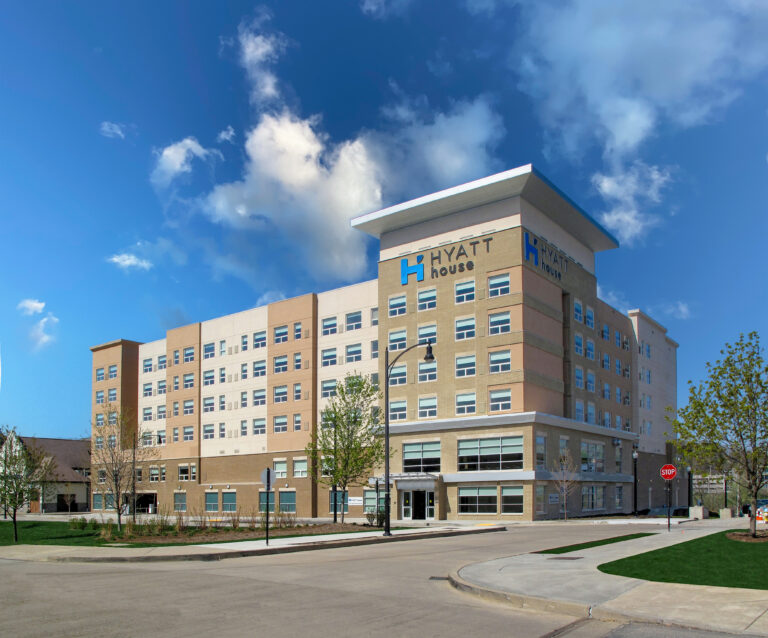 Exterior view of a multi-story Hyatt House hotel building under a blue sky with clouds.