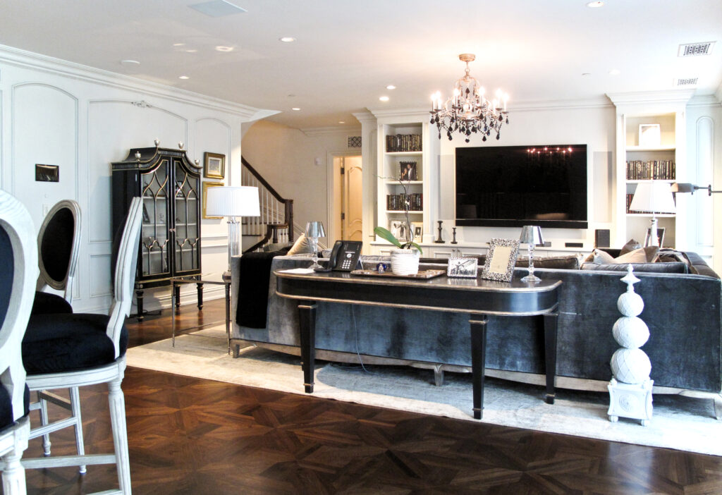 A living room with a grey sofa, a console table holding a telephone and decor, a wall-mounted television, and a dark wood floor.