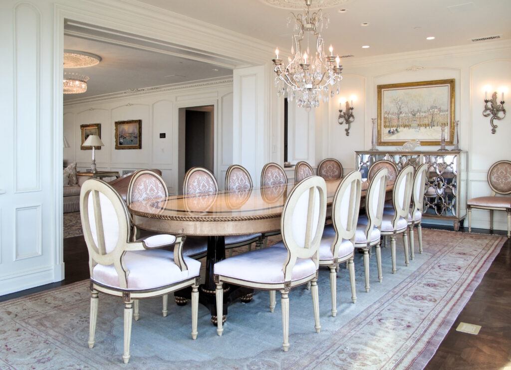 Formal dining room with an oval wooden table, twelve upholstered chairs, a crystal chandelier, and a mirrored sideboard.