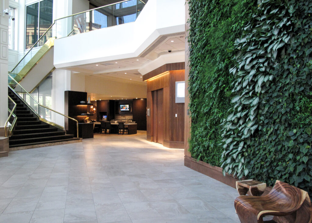 A modern building lobby featuring a tall vertical garden wall, a carpeted staircase with brass railings, and a view into a lounge area.
