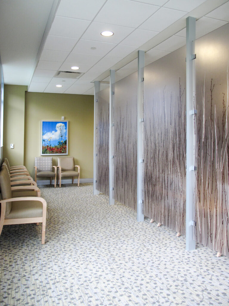 A waiting room with a row of chairs along a wall and privacy screens featuring a decorative branch pattern.
