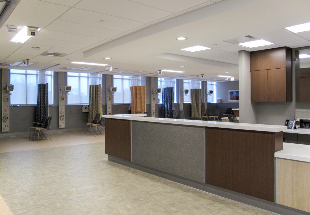 A hospital recovery ward featuring a central nurse’s station and multiple partitioned patient bays with chairs and medical equipment.