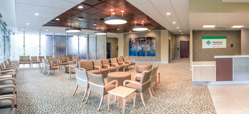 Waiting room for Allegheny Health Network Surgery Center with several armchairs, circular ottomans, and a reception desk.