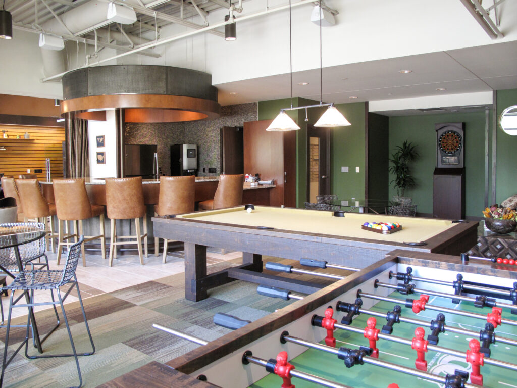 A game room featuring a foosball table, a pool table, and a bar area with stools.