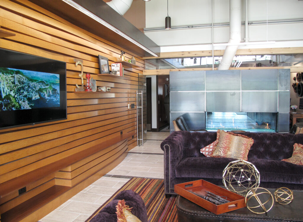 Living room with a wood-paneled wall, television, velvet sofa, and metal-paneled fireplace.