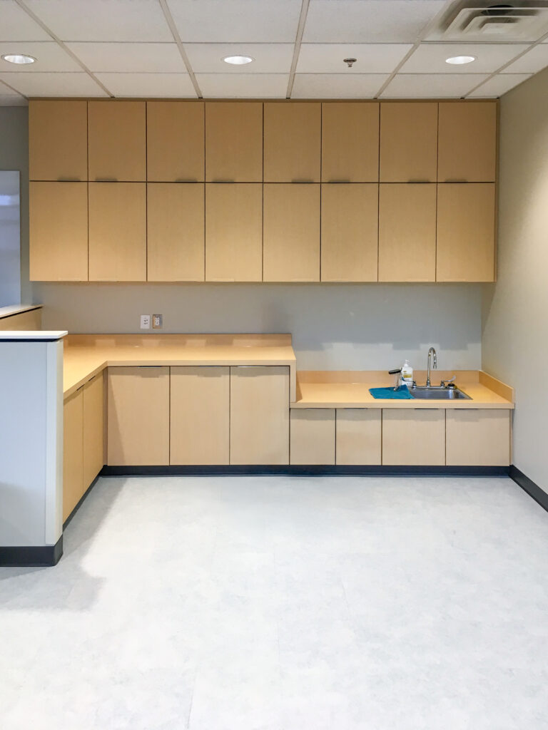 L-shaped light wood cabinets and countertops with a built-in sink in a room with a drop ceiling.