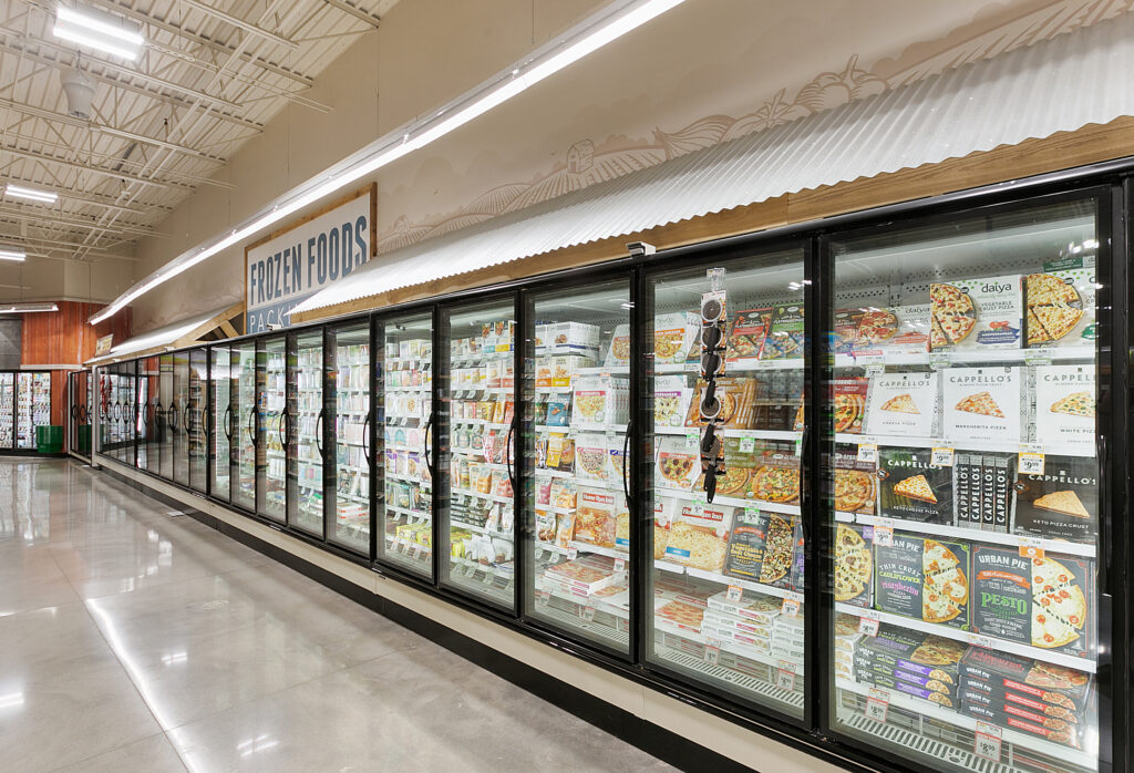 A long aisle of refrigerated glass-door display cases filled with frozen pizzas in a grocery store.