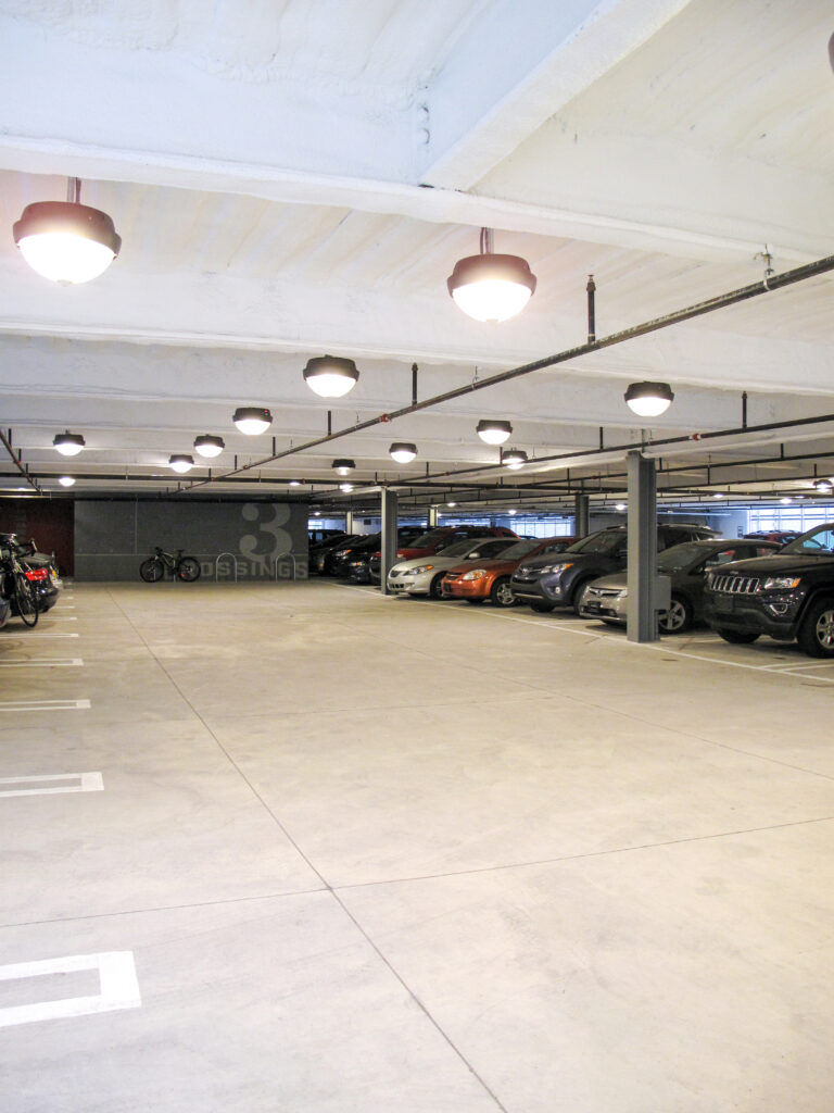 Indoor parking garage with rows of parked cars and ceiling-mounted dome lights.