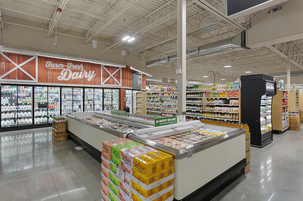 Grocery store aisle featuring a “Farm-Fresh Dairy” section, refrigerated display cases with frozen foods, and stacks of LaCroix sparkling water.