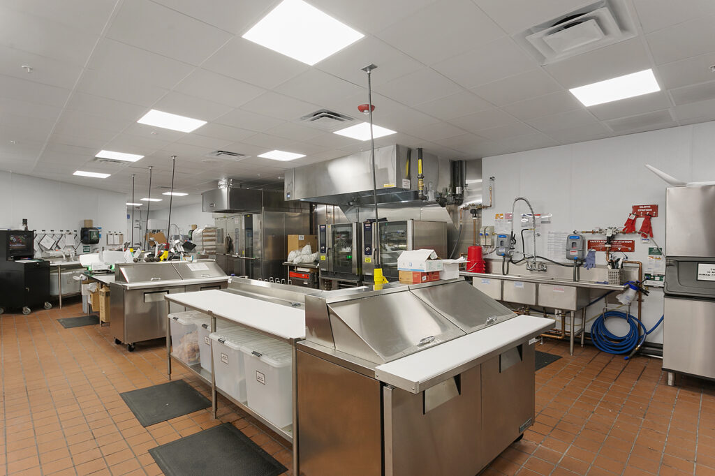 Commercial kitchen with stainless steel prep tables, ovens, and a three-compartment sink.