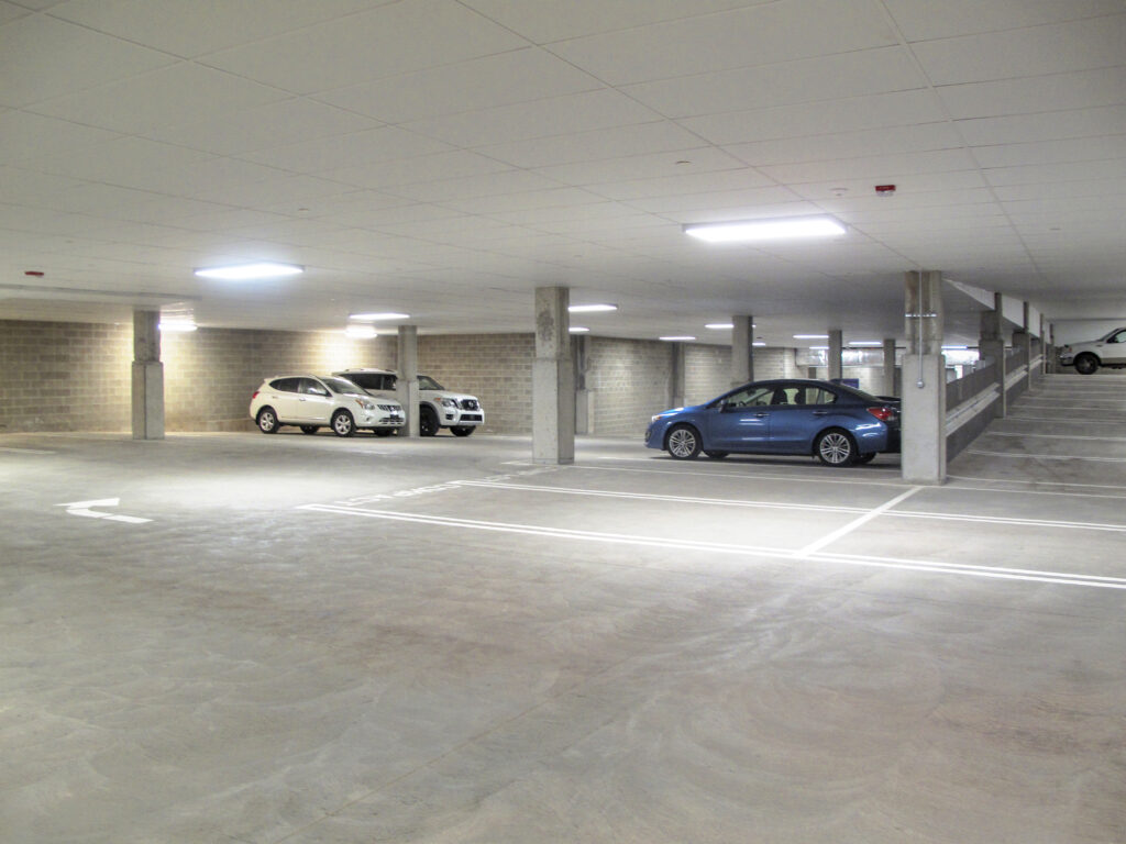 An underground parking garage with two white SUVs parked in the back and a blue sedan parked in the foreground.