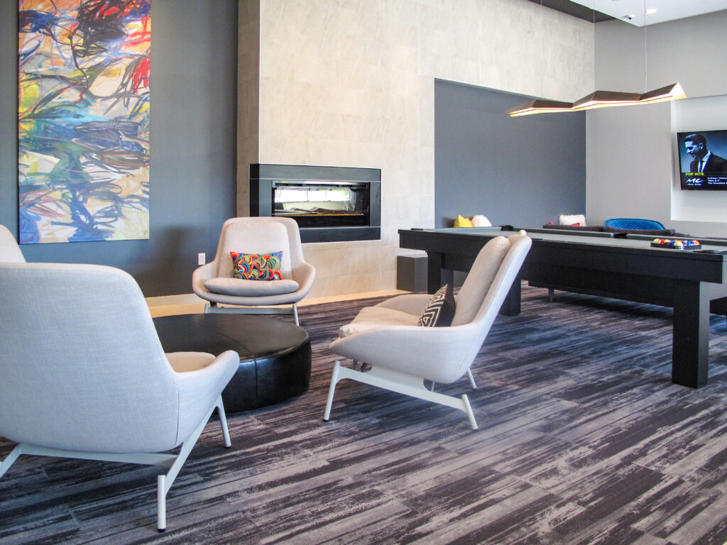 A lounge area with three armchairs, a round ottoman, a fireplace, and a pool table.