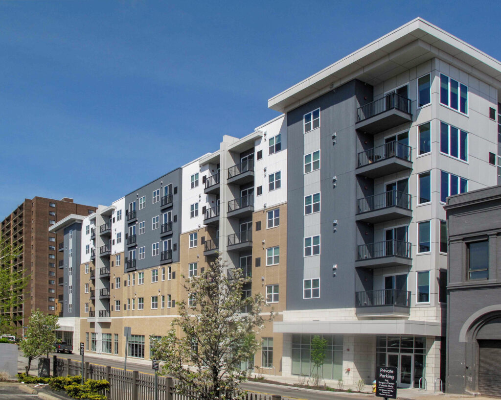 A multi-story modern apartment building featuring a mix of grey, white, and tan exterior panels with private balconies.