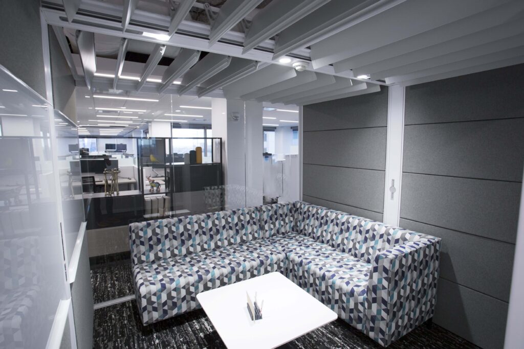 Small office meeting nook with a blue and white geometric pattern sectional sofa, a white square coffee table, and gray acoustic wall panels.