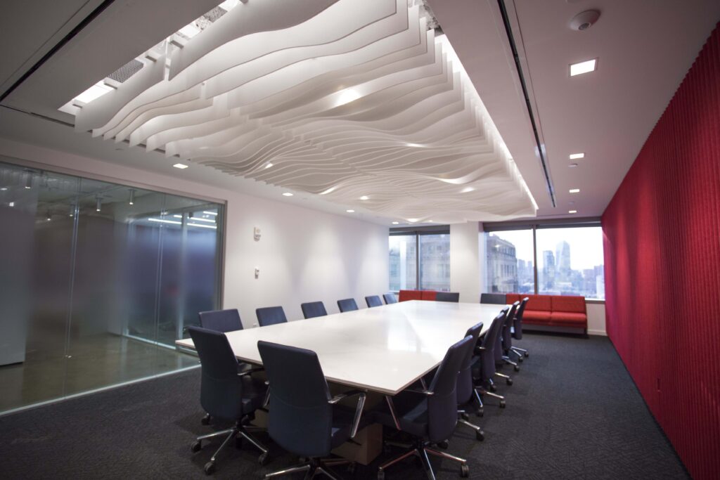 Conference room with a large white table, dark chairs, and a sculptural wavy white ceiling feature.