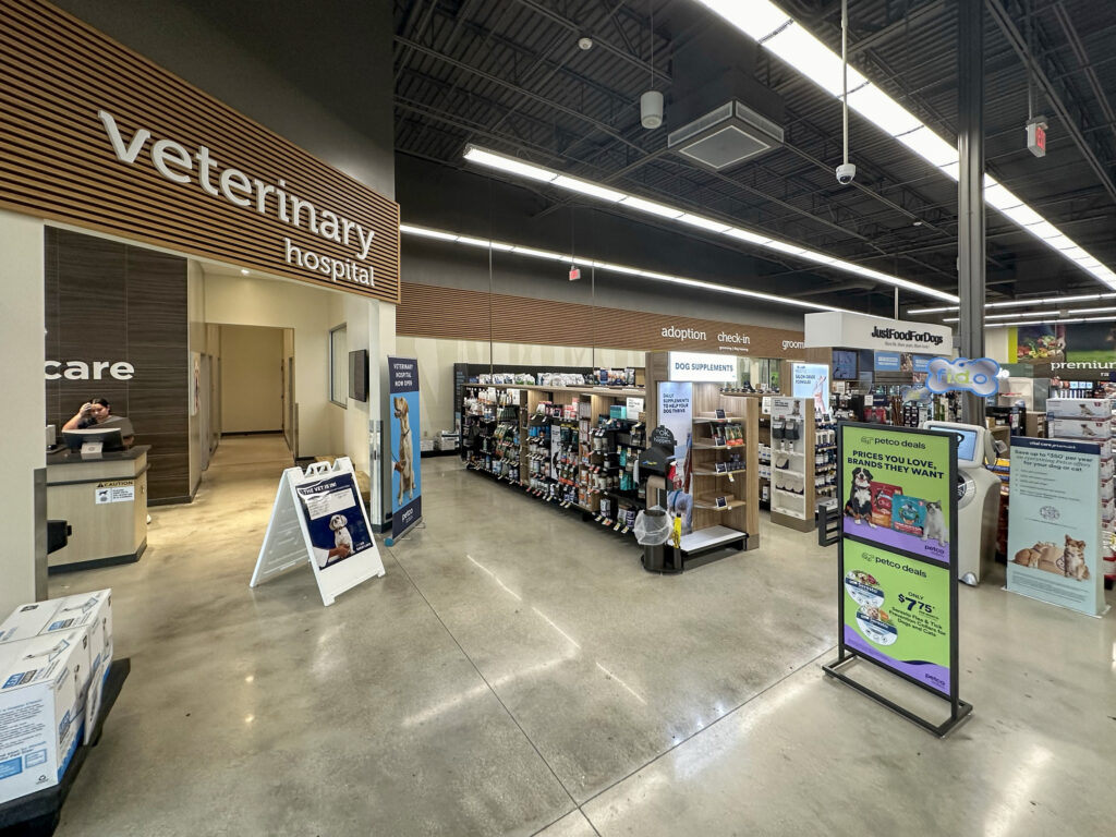 Interior view of a pet store showing a veterinary hospital entrance, aisles of pet supplies, and informational signage for grooming and adoption services.