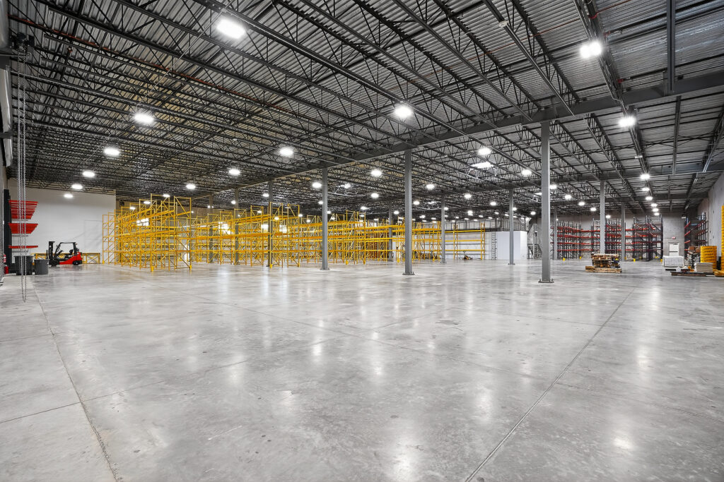 Large, empty warehouse space with high ceilings, industrial lighting, and rows of yellow metal shelving.