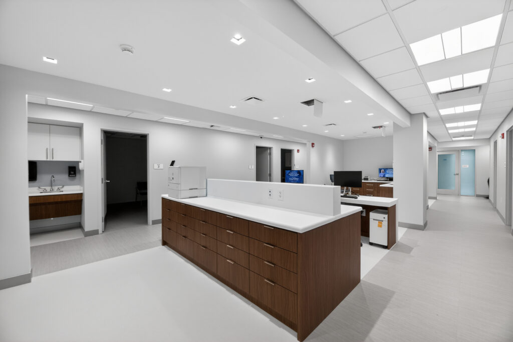 A modern medical office reception area with a central wooden desk, white countertops, and hallways leading to examination rooms.