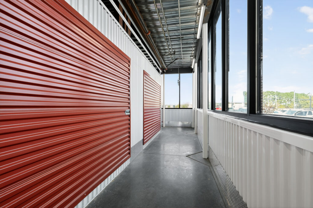 A hallway of red and white metal storage units with a row of windows looking out to a parking lot.
