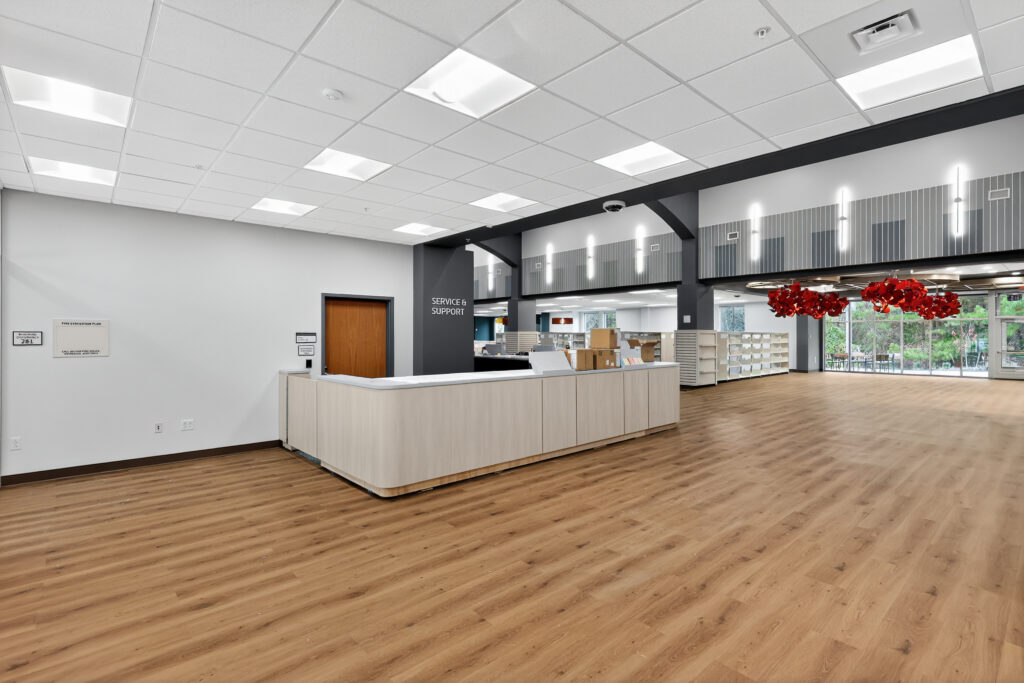 A service and support desk in a spacious, modern lobby with wood-look flooring and hanging red art installations.