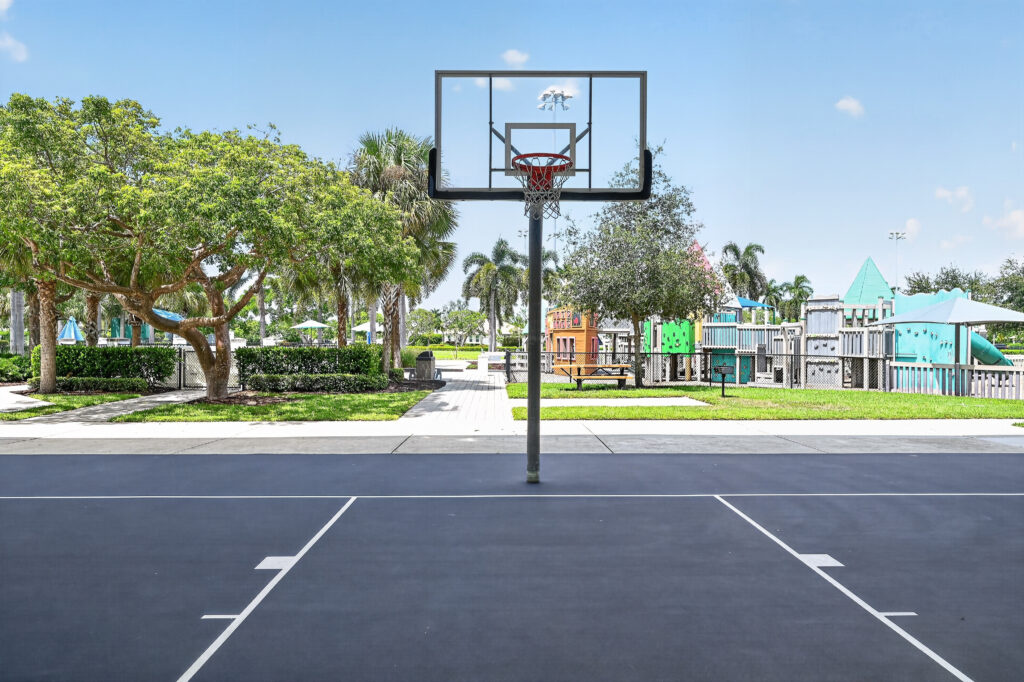 A basketball hoop on a court in a park with a playground in the background.