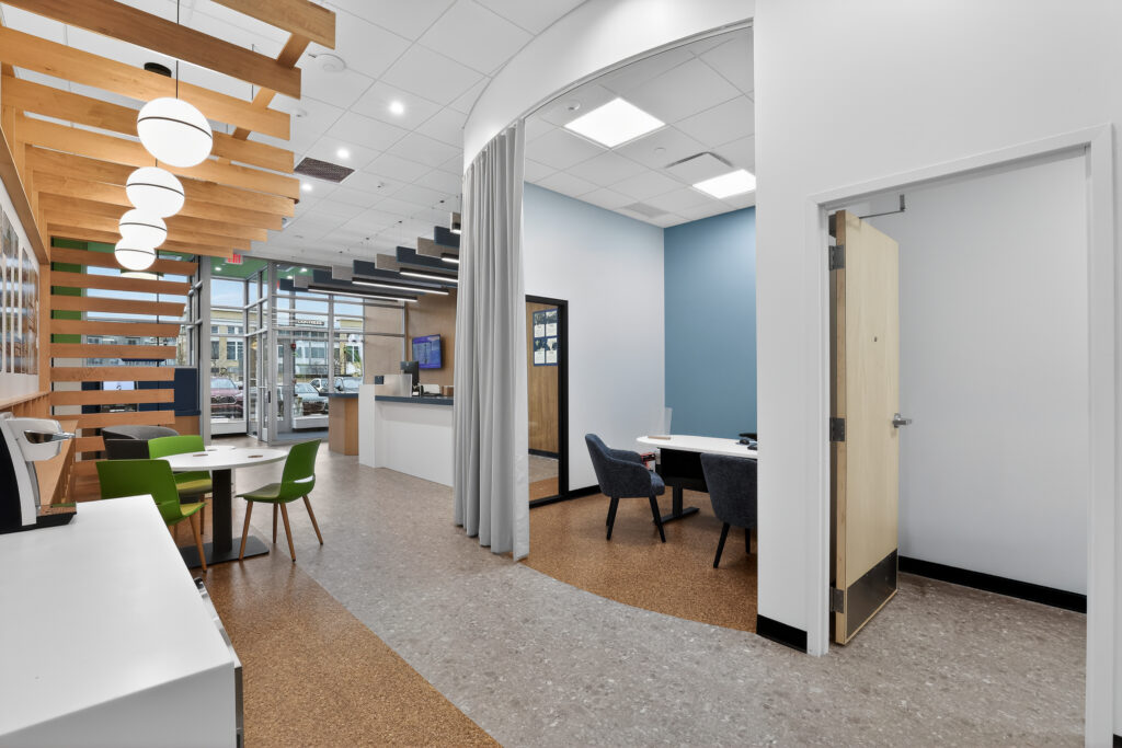 Office lobby with a waiting area featuring green chairs, a reception desk, and a private office space enclosed by a grey curtain.