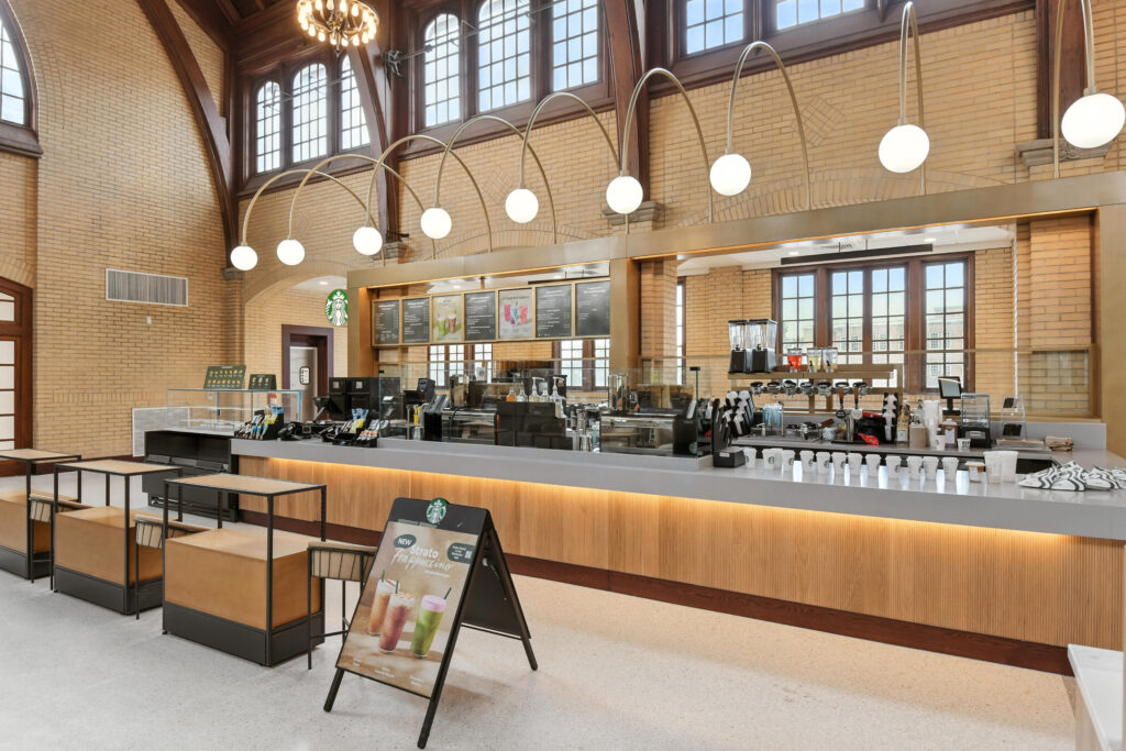 Starbucks coffee shop interior featuring a long service counter, menu boards, and a promotional sandwich board for Frappuccinos.