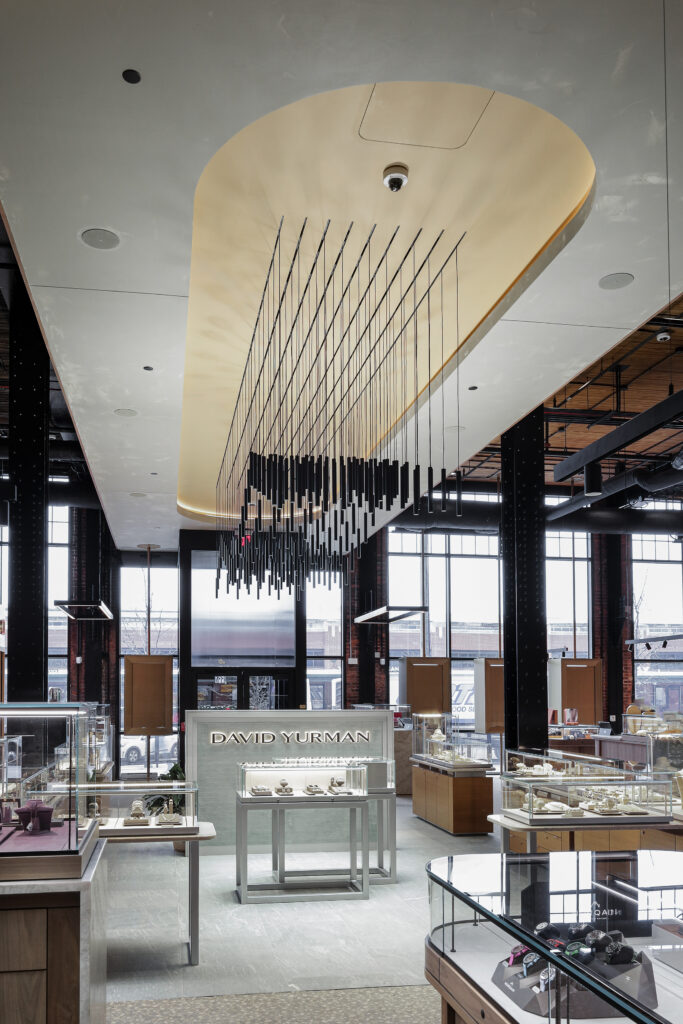 Interior of a David Yurman jewelry store with glass display cases and a decorative ceiling fixture of hanging black rods.