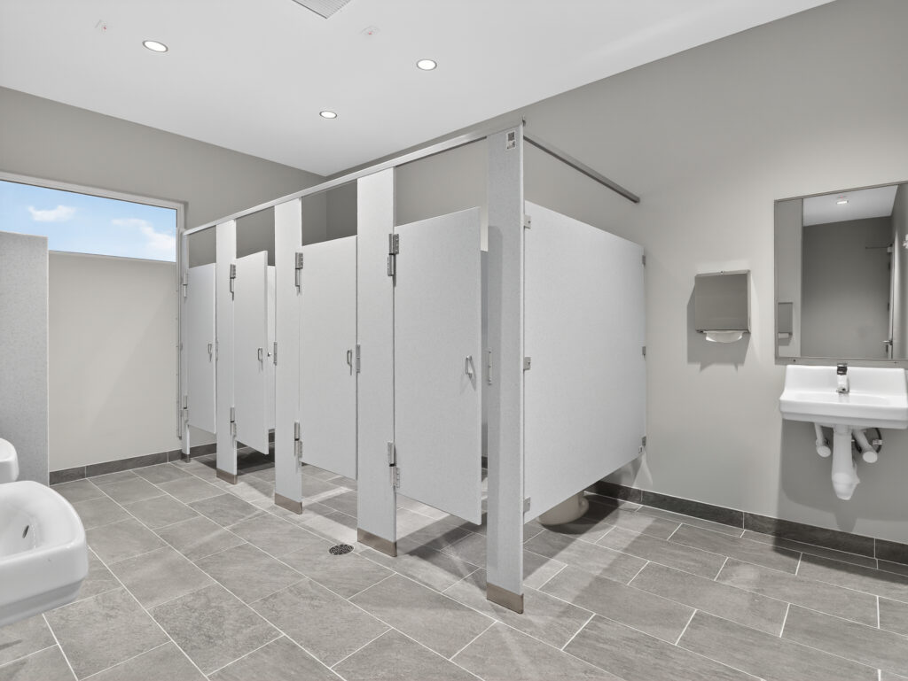 A public restroom with a row of four stalls, a wall-mounted sink, and a paper towel dispenser.