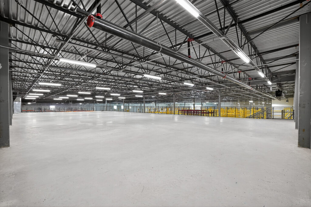 Empty industrial warehouse with a high, exposed steel ceiling and polished concrete floor.